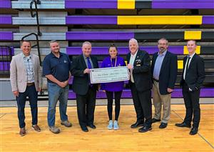 Jamie Oshel holding a novelty check & SHEF Board smiling for the Teacher Excellence Grant presentation at SHHS